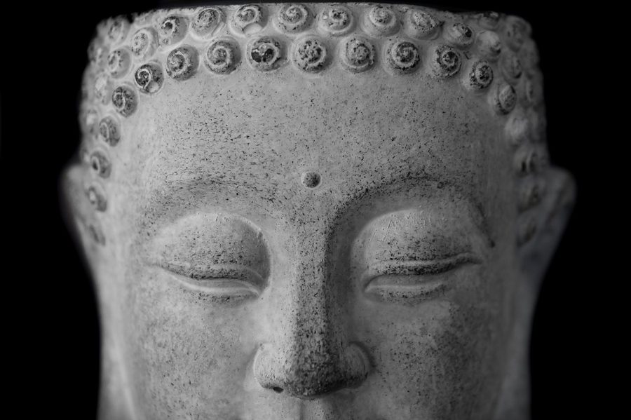 The carved face of a stone Buddha in soft monochrome light
